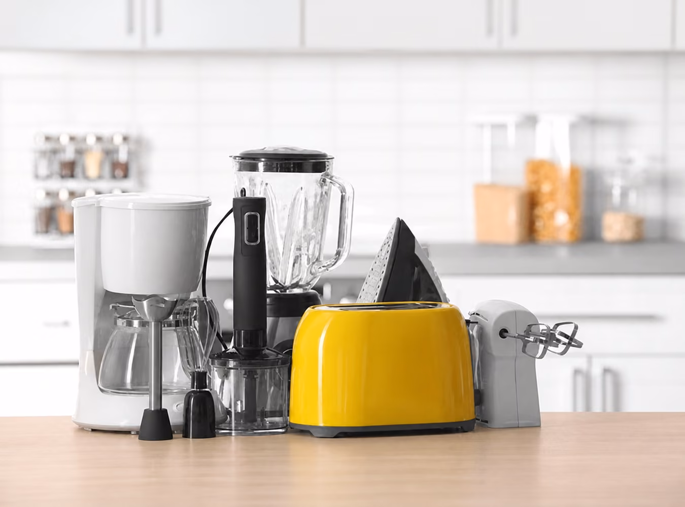 Coffee maker, blender, toaster, iron, and hand mixer arranged on a kitchen worktop